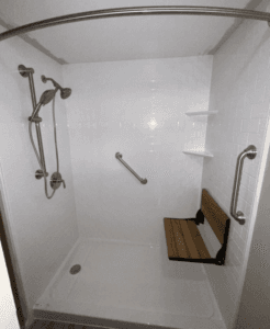 a newly remodeled shower with white surround, a shower chair, and grab bars